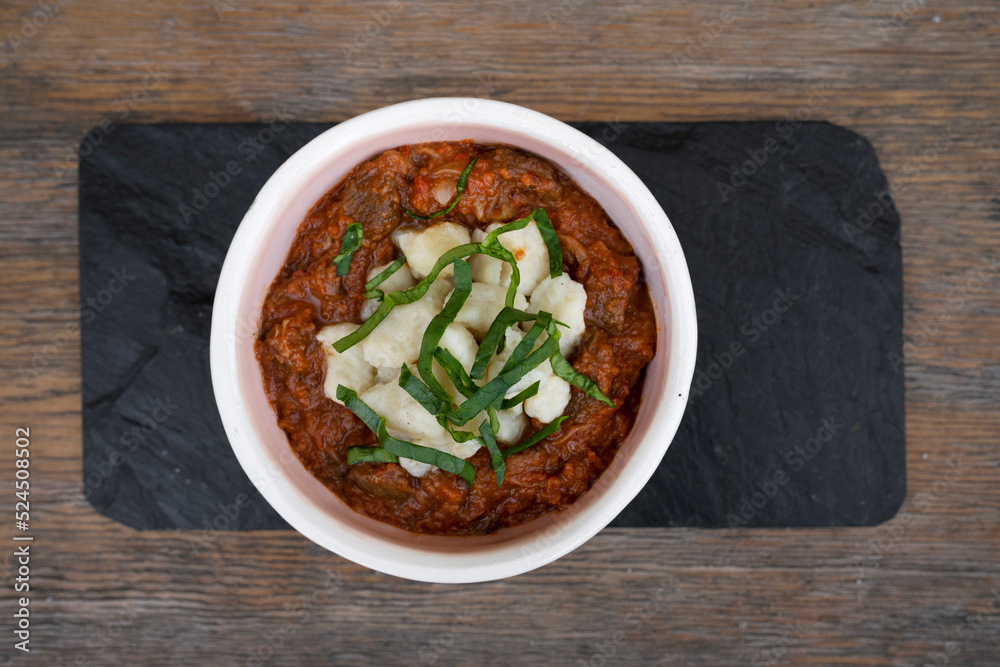 Top view of traditional goulash stew, with veil and gnocchi in a bowl on the wooden table. Top view of traditional goulash stew, with veil and gnocchi in a bowl on the wooden table.