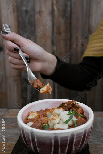 Eating at the restaurant. Closeup view of a woman holding a fork with having goulash stew made with veal, sauce and gnocchi.