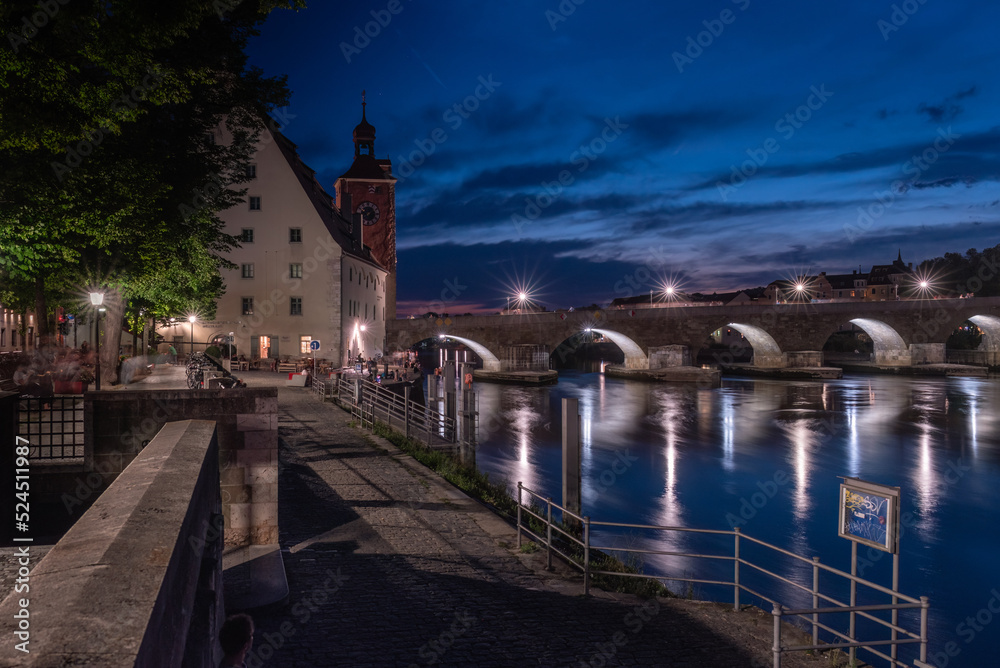 Steinerne Brücke nachts beleuchtet mit Spiegelung in Regensburg mit Brückturm