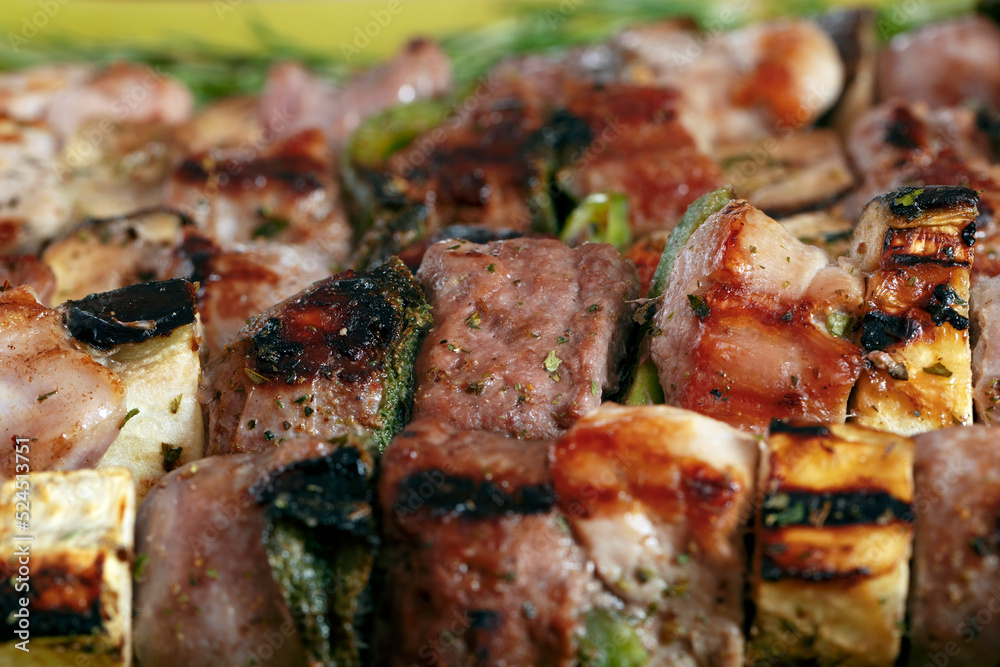 Macro close up of baked meat skewers on a green dish with sage leaves, salt and mixed pepper.