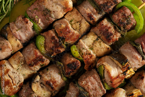 Macro close up of baked meat skewers on a green dish with sage leaves, salt and mixed pepper.