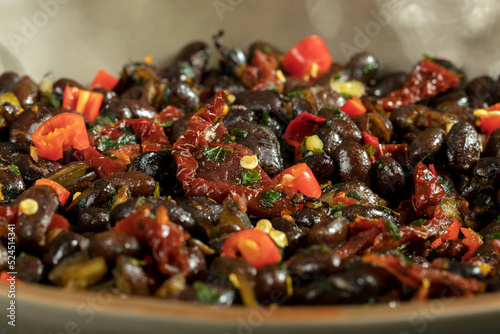 Macro close up of black beans with dried tomatoes and red Cayenne chili peppers in a brown dish.