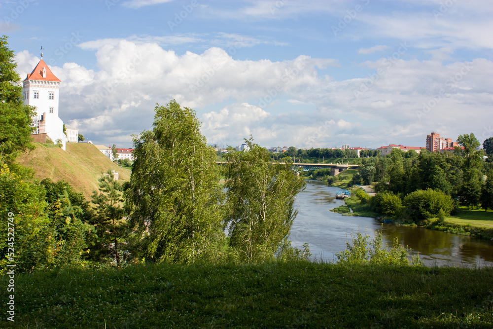 Obraz premium Neighborhood of Grodno, Belarus. Summer landscape overlooking the Neman River and the old castle on a high hill surrounded by green trees in the sun.