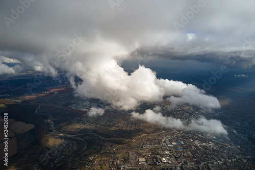Aerial view from airplane window at high altitude of distant city covered with white puffy cumulus clouds © bilanol