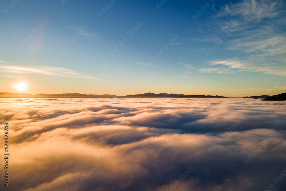 Fototapeta premium Aerial view of vibrant yellow sunrise over white dense clouds and distant mountains on horizon