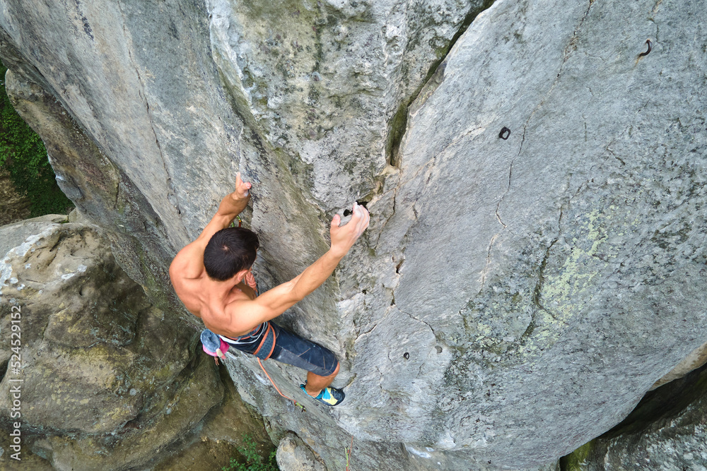 Young man climbing steep wall of rocky mountain. Male climber overcomes challenging route. Engaging in extreme sport concept Young man climbing steep wall of rocky mountain. Male climber overcomes challenging route. Engaging in extreme sport concept