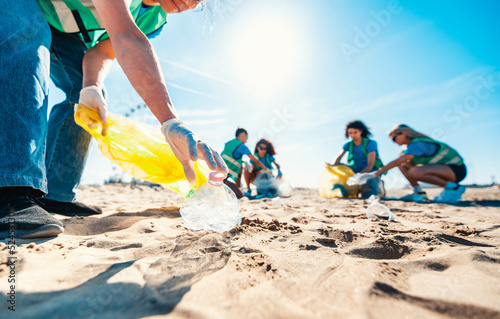 Group of eco volunteers picking up plastic trash on the beach - Activist people collecting garbage protecting the planet - Ocean pollution, environmental conservation and ecology concept. photo