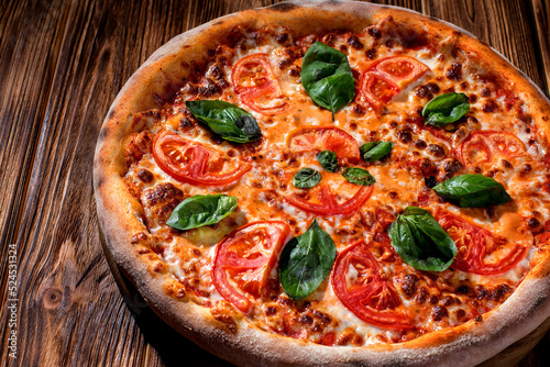 Delicious fragrant pizza with mozzarella, tomatoes and basil with tomato sauce on woden background