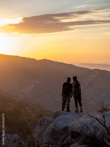 Vertical image of young native friends standing at the edge of a cliff watching the sun set