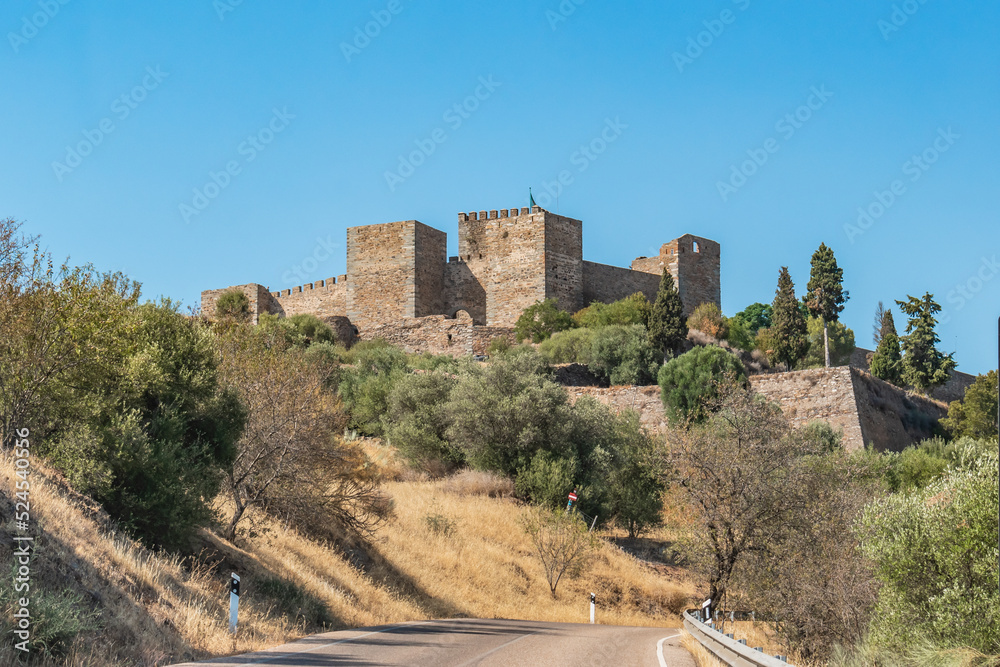 Road and hillside with dry herbs and trees and Monsaraz fortress castle in the background, Alentejo PORTUGAL