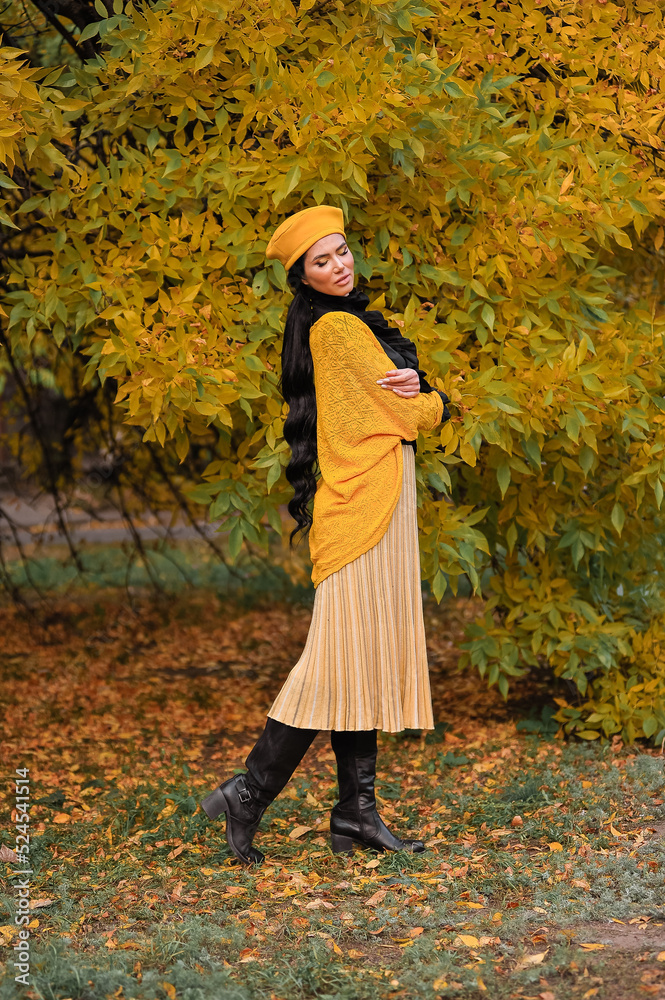 a beautiful brunette with makeup in a yellow beret and yellow jacket walks in the park in autumn. a beautiful brunette with makeup in a yellow beret and yellow jacket walks in the park in autumn.