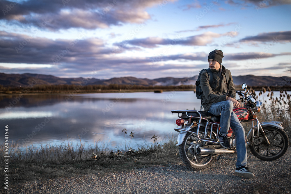 Fototapeta premium A man sits on a motorcycle in the mountains by a river, embodying adventure and the great outdoors.