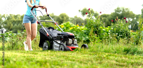 a girl mows the lawn with a lawn mower