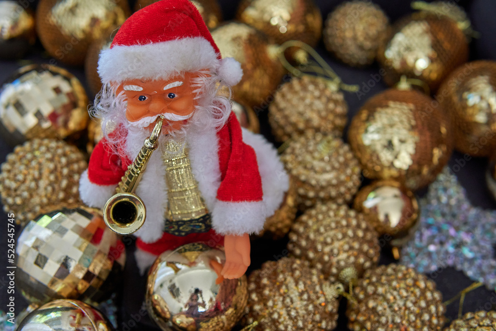 little doll of Santa Claus with saxophone on front with golden Shimmering balls in background. Christmas decoration