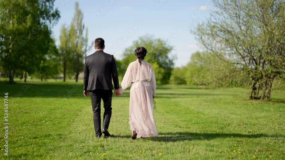 happy loving husband and wife are walking together in beautiful sunny garden in spring day, rear view happy loving husband and wife are walking together in beautiful sunny garden in spring day, rear view