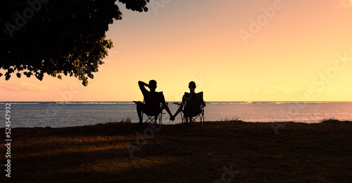 Silhouette of happy couple man and woman enjoying the nature sunset sitting holding hands 