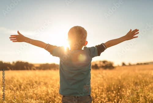 It's a beautiful life! Child standing in a field at sunset having feelings of freedom, hope, and happiness 