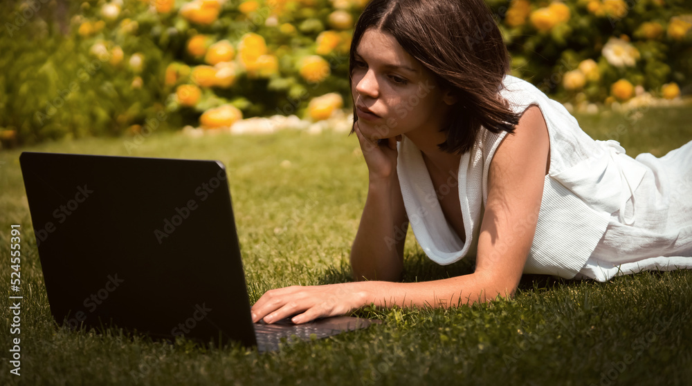 A young girl in a white dress is working on a laptop.