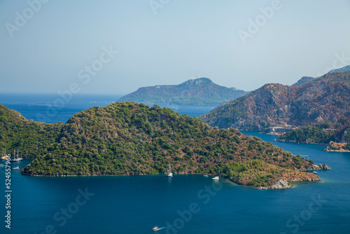 Marmaris, Turkey – Beautiful view of the islands and the boats on the crystal clear water of the bay at sunny day with its misty green mountains at background and the blue bay.