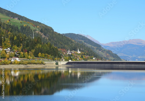 Zoggler Stausee mit Staumauer und Blick auf St. Walburg im Ultental in Südtirol, herbstlicher Blick aus dem Tal	