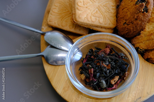 Dried tea leaves with tea pot and cookies on a gray table with spoons and wooden board photo