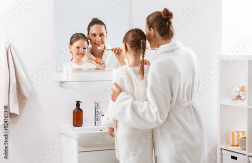 beauty, hygiene, morning and people concept - happy smiling mother and little daughter with toothbrushes brushing teeth at bathroom