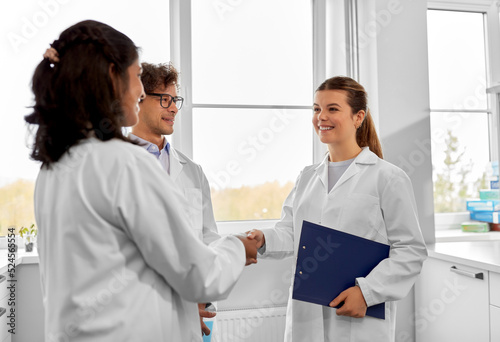 science, work and people concept - international group of happy scientists shaking hands in laboratory