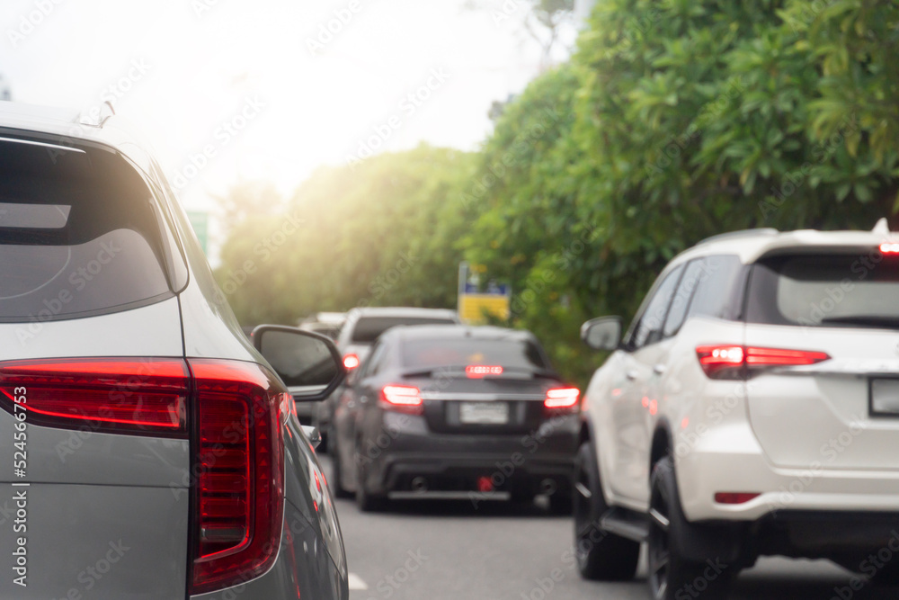 Rear side of gray car on the asphalt road heading towards the goal of the trip. Traveling for work during rush hour. Environment blurred of other cars in the city. Island of green trees beside.