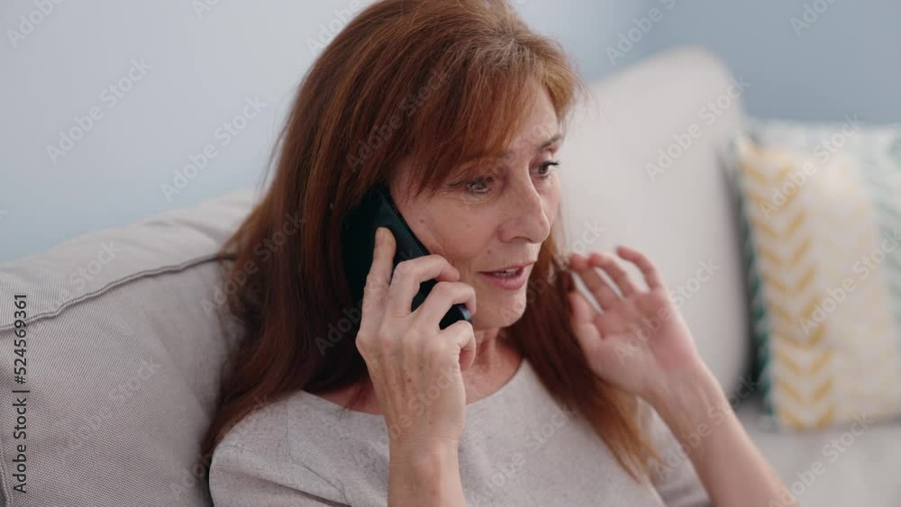 Middle age woman talking on the smartphone sitting on sofa at home Middle age woman talking on the smartphone sitting on sofa at home