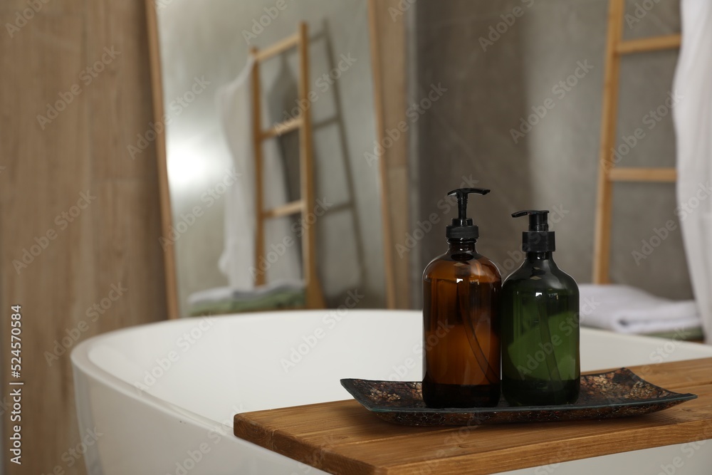 Wooden bath tray with bottles of shower gels on tub indoors, space for text Wooden bath tray with bottles of shower gels on tub indoors, space for text