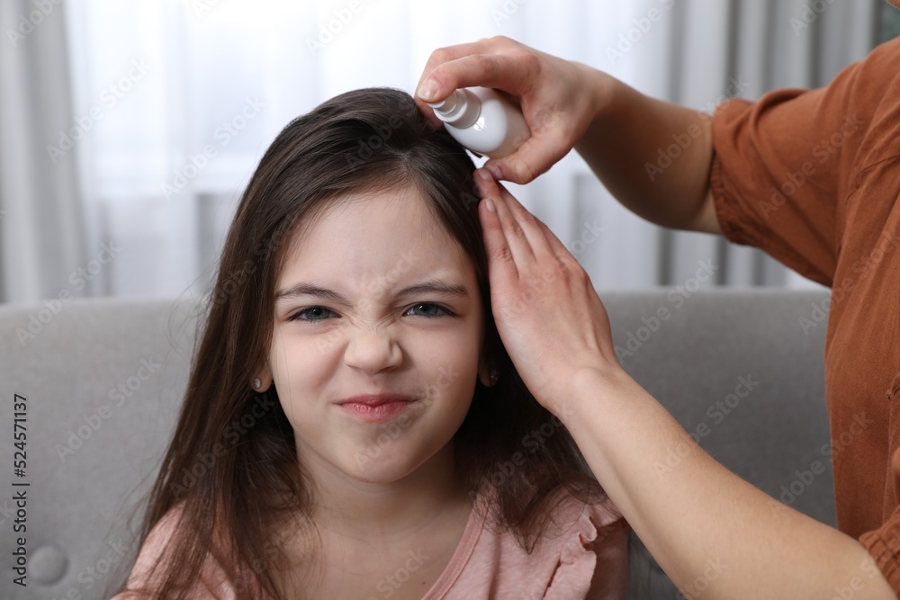 Mother using lice treatment spray on her daughter's hair indoors Mother using lice treatment spray on her daughter's hair indoors