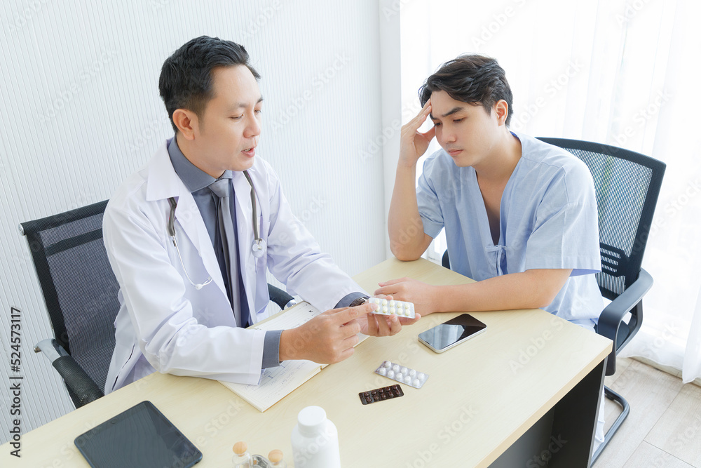 Male doctor and young male patient while consult and .explain. Doctor and patient sitting together at table in clinic Male doctor and young male patient while consult and .explain. Doctor and patient sitting together at table in clinic