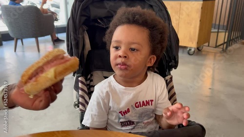 Adorable and expressive afro european two year old child tasting a delicious ham and cheese bagel in a cafeteria. photo