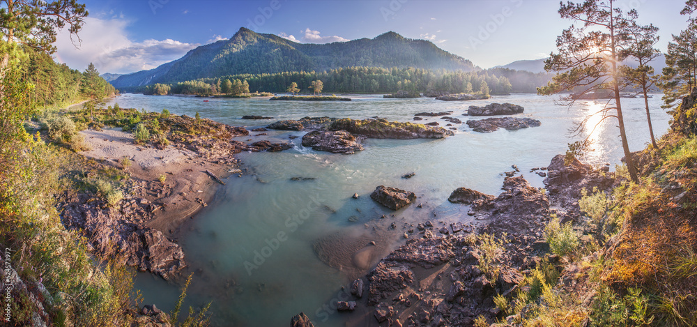 View of a mountain river in the evening light, the setting sun, a rocky shore and a forest