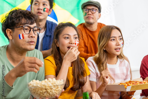 Group of Asian man and woman friends watching soccer games world cup competition on television with eating snack together at home. Sport fans people shouting and celebrating sport team victory match.