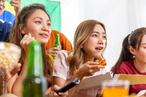 Group of Asian man and woman friends watching soccer games world cup competition on television with eating snack together at home. Sport fans people shouting and celebrating sport team victory match. photo