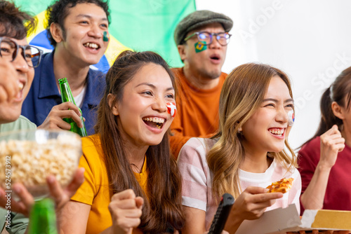 Group of Asian man and woman friends watching soccer games world cup competition on television with eating snack together at home. Sport fans people shouting and celebrating sport team victory match.
