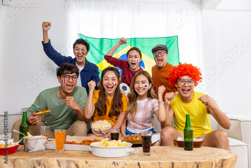 Group of Asian man and woman friends watching soccer games world cup competition on television with eating snack together at home. Sport fans people shouting and celebrating sport team victory match. photo