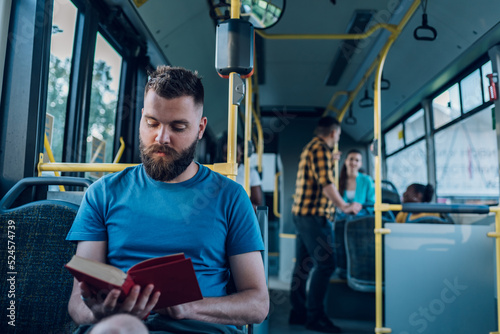 Man is riding in a bus and reading a popular fiction book