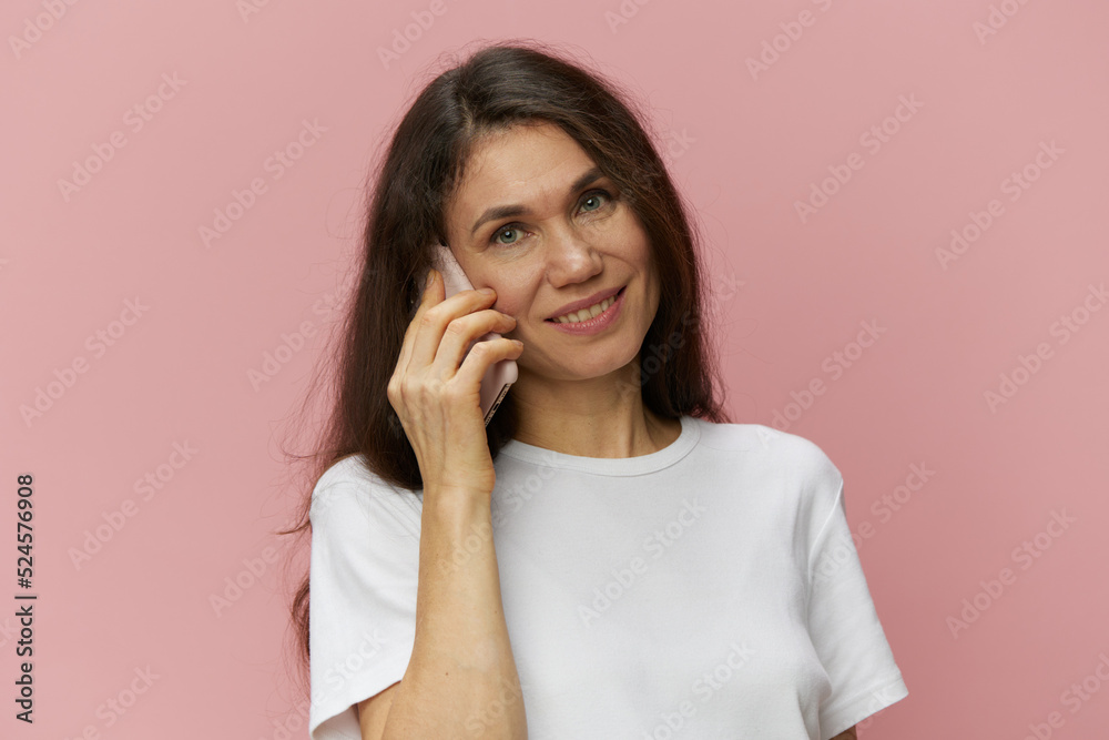 portrait of a beautiful, cute, attractive brunette woman in a light t-shirt standing on a pink background and talking on the phone, with a pleasant smile on her face portrait of a beautiful, cute, attractive brunette woman in a light t-shirt standing on a pink background and talking on the phone, with a pleasant smile on her face