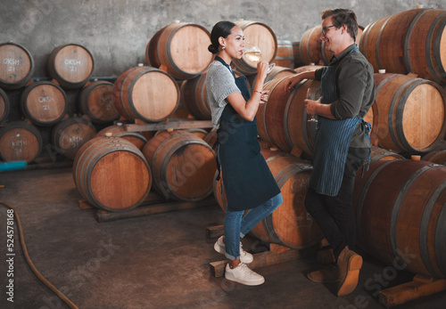 Wine distillery owners tasting the produce in the cellar standing by the barrels. Oenologists or sommeliers drinking a glass of chardonnay or sauvignon blanc inside a winery testing the quality photo