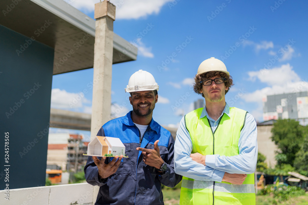 Architect and civil engineer in safety uniform holding house model of the house structure and discuss at construction site on sunny day. Renovate and construction concept. Specialists home project Architect and civil engineer in safety uniform holding house model of the house structure and discuss at construction site on sunny day. Renovate and construction concept. Specialists home project