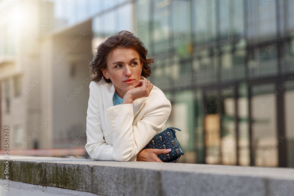 Fototapeta premium Focused woman in white suit standing near business centre. Blurred background