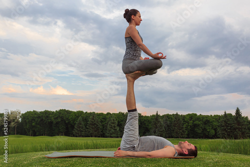 Man lying on grass and balancing woman in his feet. Young couple doing acro yoga in park photo