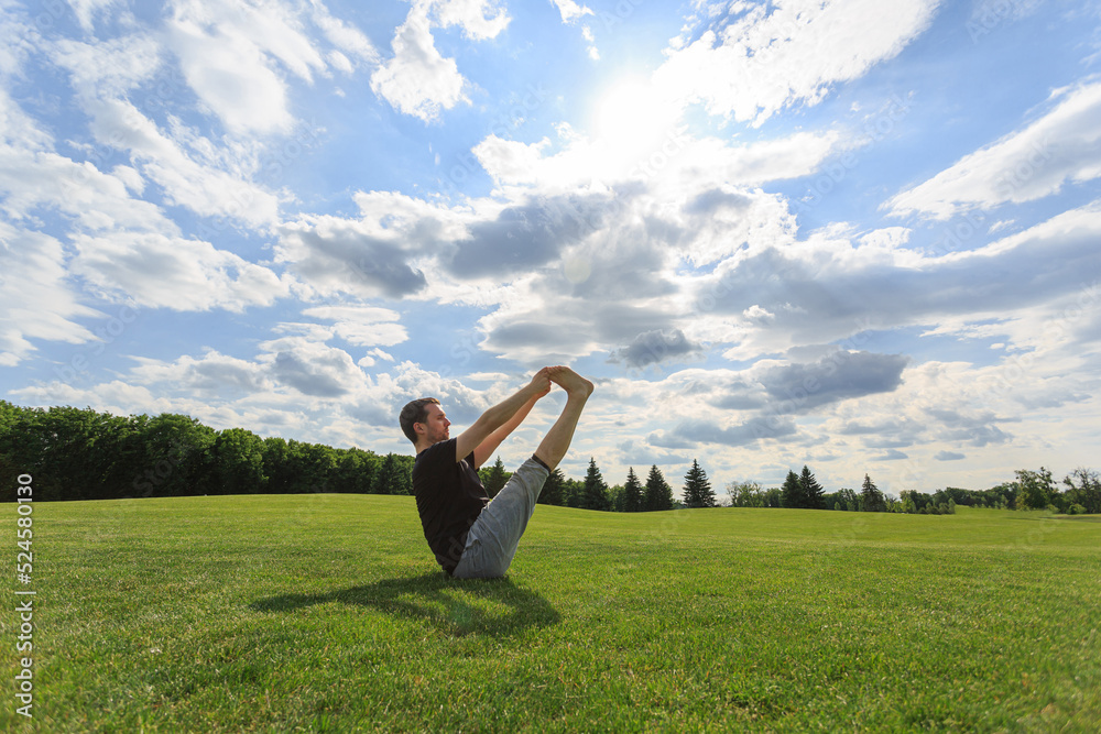Man stretching hands and legs on green grass in park. Yoga and healthy lifestyle concept Man stretching hands and legs on green grass in park. Yoga and healthy lifestyle concept