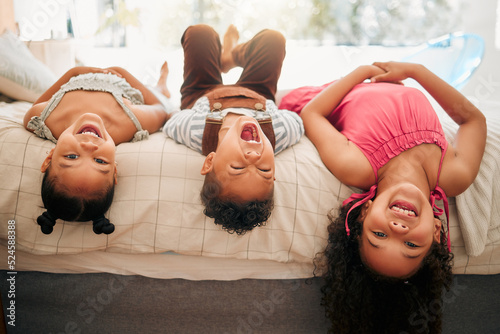 Silly kids playing upside down on bed enjoy and having fun together in parents bedroom. Happy children or siblings bonding and enjoying childhood together at cozy, warm and comfortable family home
