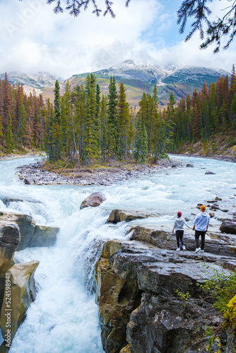 Sunwapta Falls Jasper National Park, Canada. The Canadian Rockies during the Autumn fall season. A couple of men and women visiting Sunwapta falls standing on the edge of the rocks by the river photo