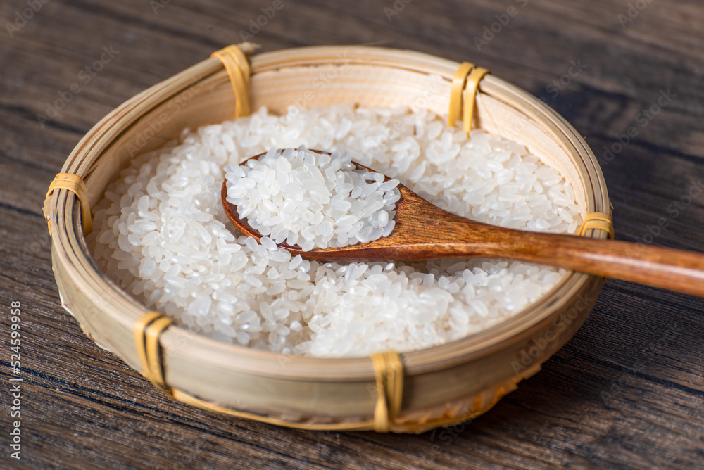 Wooden spoon full of rice in bamboo basket full of rice grains on table