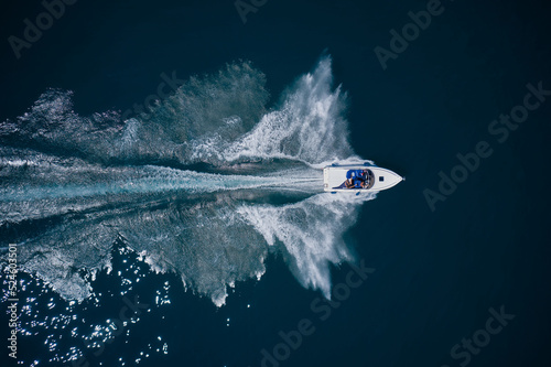 White big speedboat moves fast on dark water top view. Luxury white boat with people fast movement on the water top view.