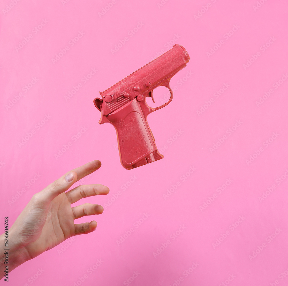 Hand and Levitating pink gun on pink background. Minimalistic still